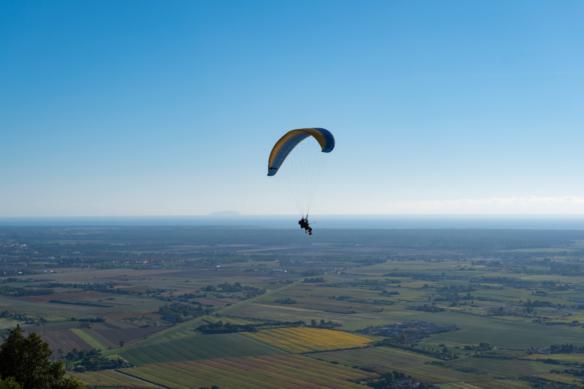 paraglider flying over the countryside with the sea on the horizon